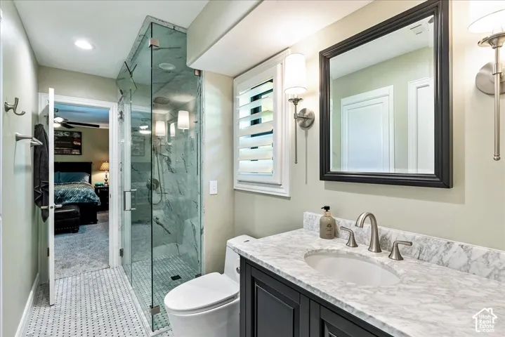 Glass-enclosed shower with tiled walls, dual wall sconces, wood-finish vanity with a stone countertop, and plantation shutters