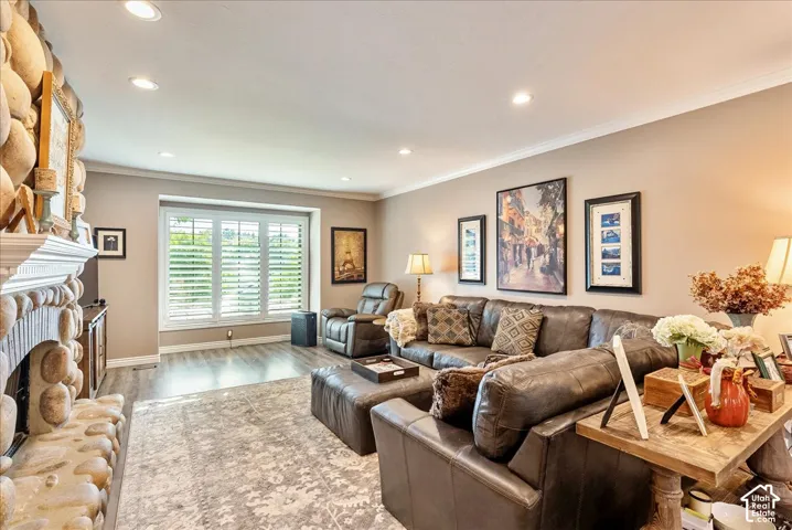 Stone-clad fireplace with mantel, recessed lighting, crown molding, wood-finish flooring, and window with plantation shutters