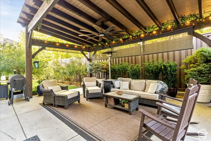 Covered patio featuring a wood-beam pergola, ceiling fan, privacy screens, and concrete flooring