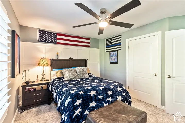 White paneled accent wall, neutral carpeting, ceiling fan with integrated lighting, wood-finish headboard, and white interior doors