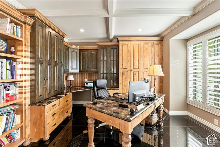Built-in wood cabinetry, coffered ceiling, black tile flooring, wood-finish desk, and plantation shutters