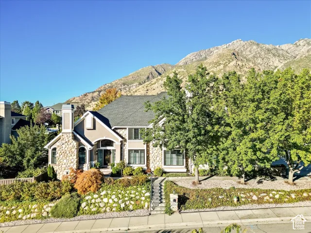 Stone facade exterior with a gabled roof, prominent chimney, mature landscaping, and an arched entry