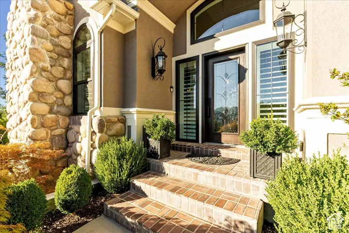 Stone veneer column, stucco exterior, decorative glass entry door, brick steps, and exterior sconce lighting