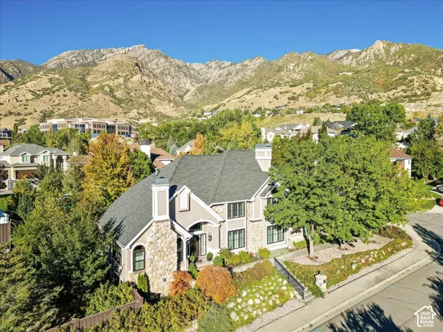 Stone and stucco exterior, multiple gables, paved driveway, mature landscaping, and mountain backdrop