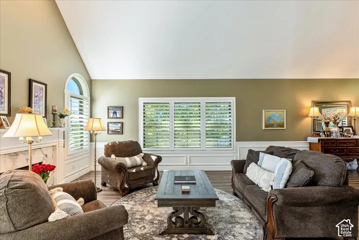 Vaulted ceiling, multiple windows with plantation shutters, fireplace with marble-finish surround, wood-finish flooring, and decorative wall molding