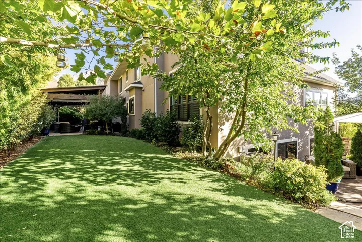 Expansive lawn area with lush artificial turf, bordered by mature trees and established landscaping