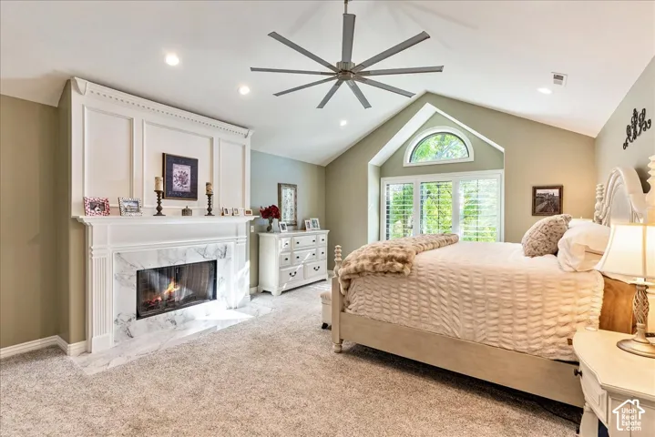 Vaulted ceiling with an overhead fan, arched window, built-in fireplace with a white marble surround, white paneled wall accent, and recessed lighting