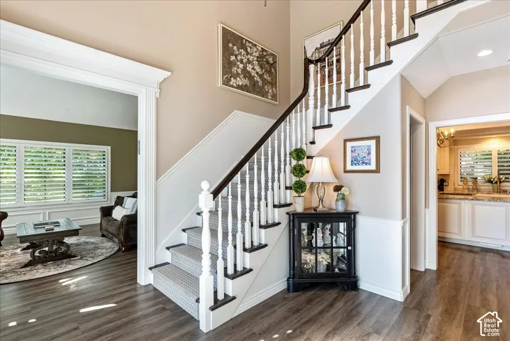 Wood-finish flooring, staircase with dark wood handrail and white balusters, wainscoting detail, custom window shutters, and recessed lighting