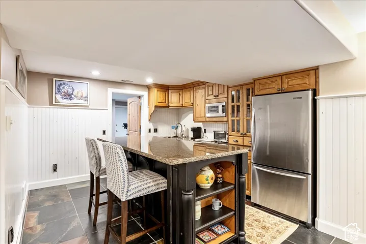Kitchenette featuring rich wood cabinetry, stainless steel appliances, a center island with a stone countertop, and slate flooring