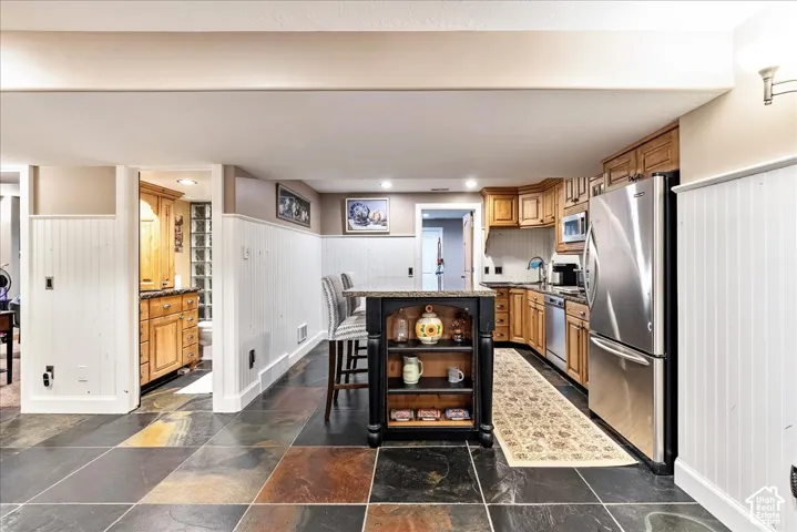Kitchenette featuring wood cabinetry, stainless steel appliances, a center island with seating, and multi-toned slate tile flooring
