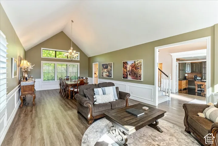 Vaulted ceiling with chandelier, light wood-finish flooring, and white wainscoting