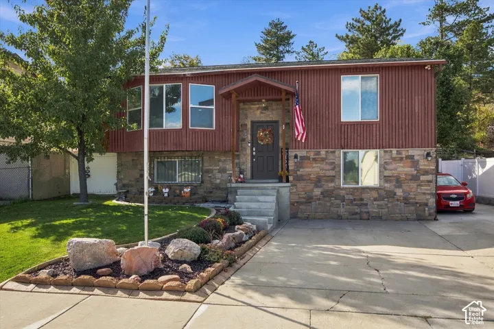 Split-level residence featuring a stacked stone and vertical siding exterior, front yard landscaping with decorative rocks, and a paved driveway
