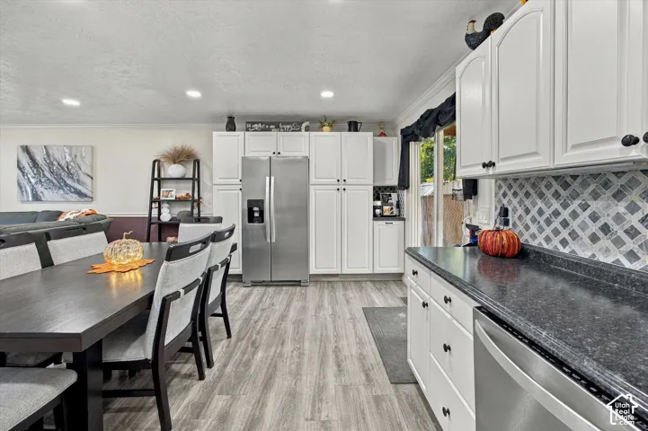 Wood-finish flooring, white cabinetry, dark countertops, tile backsplash, and stainless steel appliances