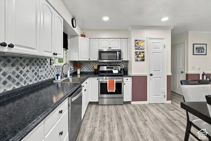 White cabinetry, stainless steel appliances, dark countertops, patterned tile backsplash, and wood-finish flooring