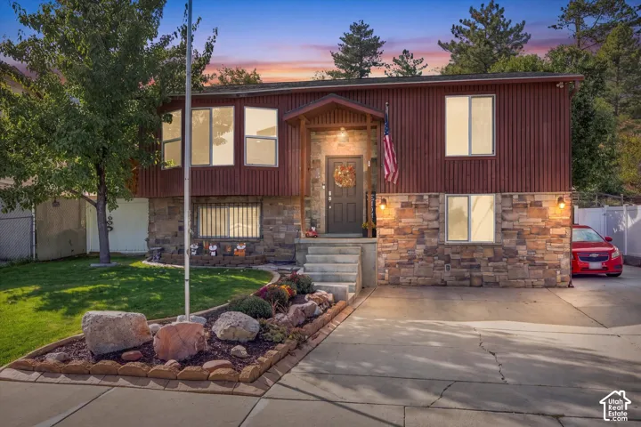 Split-level residence featuring a stone and wood-paneled exterior, concrete driveway, and a front entry with stone steps