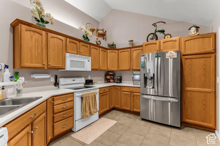 Vaulted ceiling kitchen featuring wood cabinetry, white countertops, a stainless steel refrigerator, and a white electric range