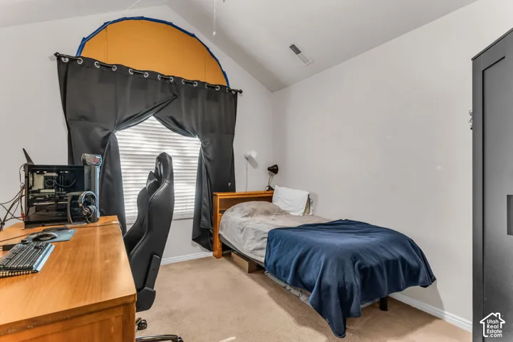Vaulted ceiling, arched window, wall-mounted light fixture, carpeted flooring, wood-finish desk