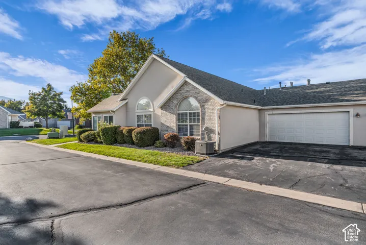 Exterior with light-colored stucco and brick accents, arched windows, an attached garage, and a paved driveway