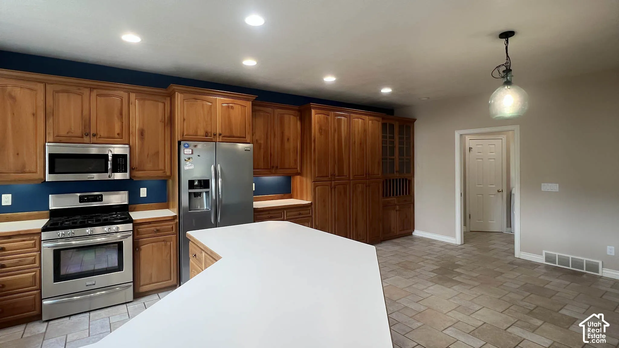 Kitchen featuring wood cabinetry, stainless steel appliances, a white island, recessed lighting, and tile flooring