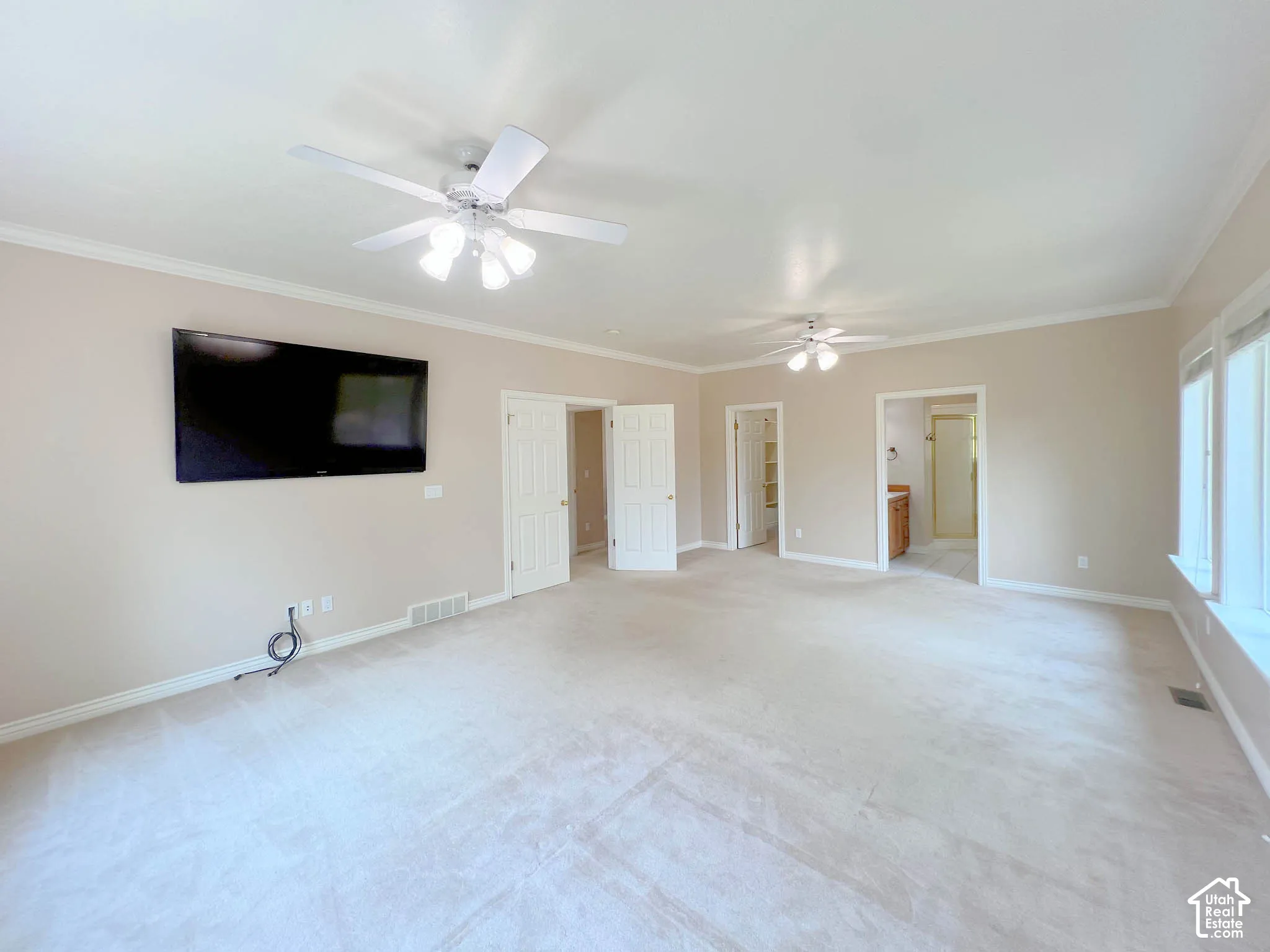 Expansive room featuring light-colored carpeting, multiple ceiling fans, and crown molding