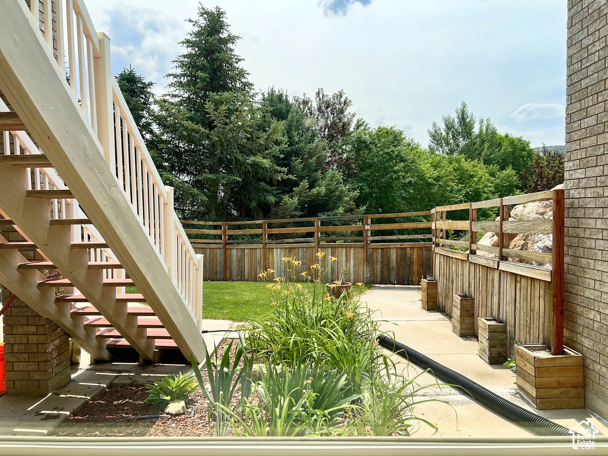 Outdoor patio with a white-railed staircase, wood-paneled fencing, and an expansive lawn
