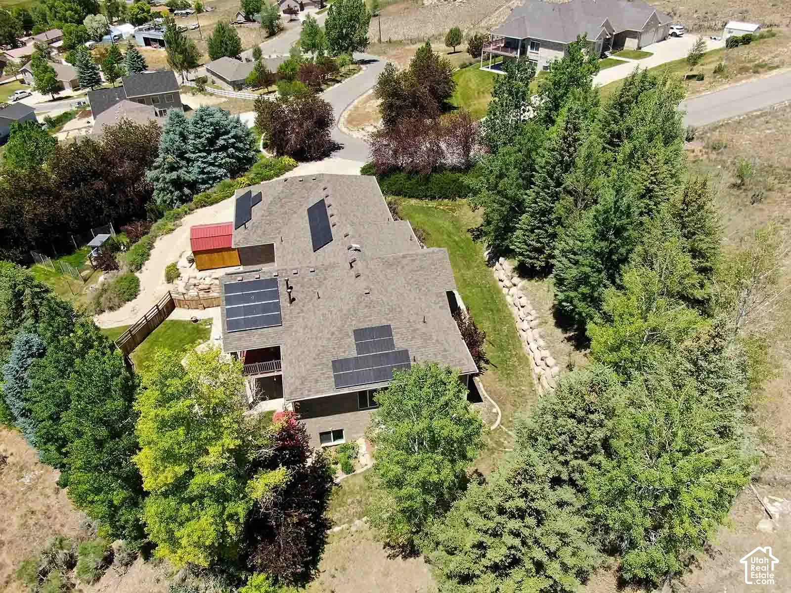Property featuring a pitched roof, multiple solar panels, and a terraced landscape with mature trees