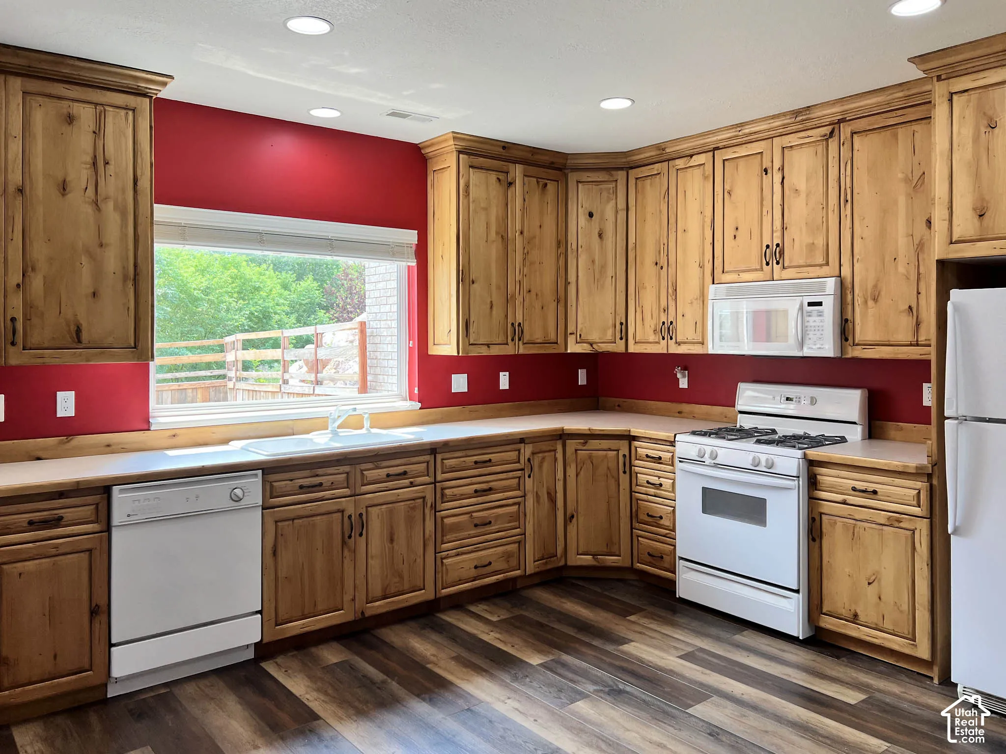 Kitchen featuring extensive wood cabinetry, wood-finish flooring, recessed lighting, and a window with a sink