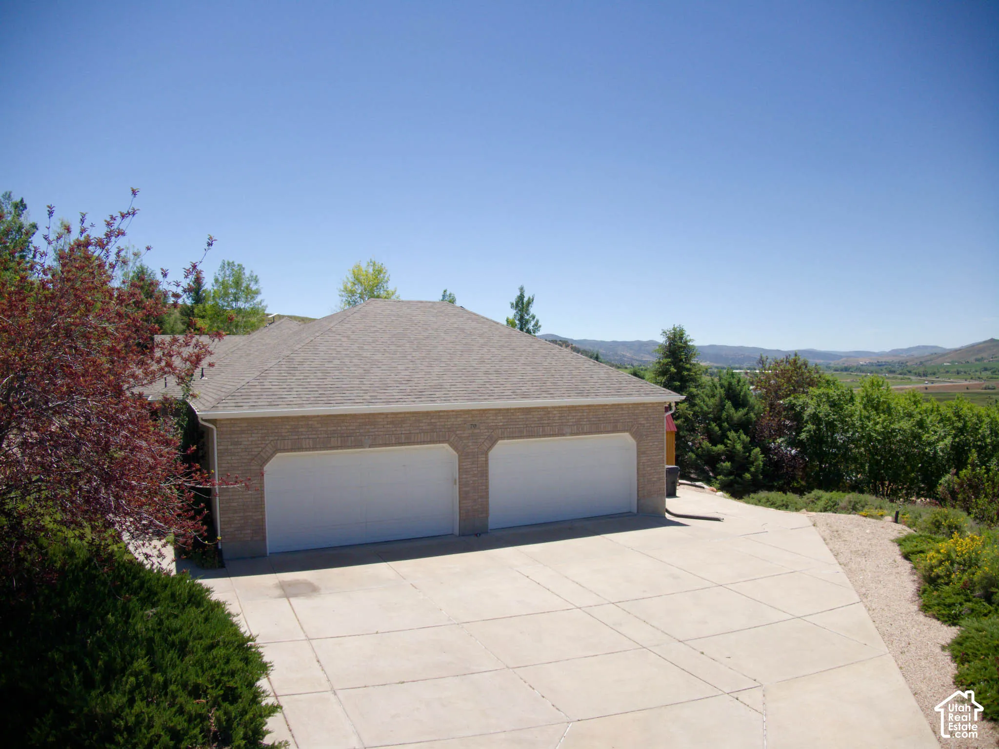 Brick exterior garage with two white garage doors, a concrete driveway, and surrounding greenery
