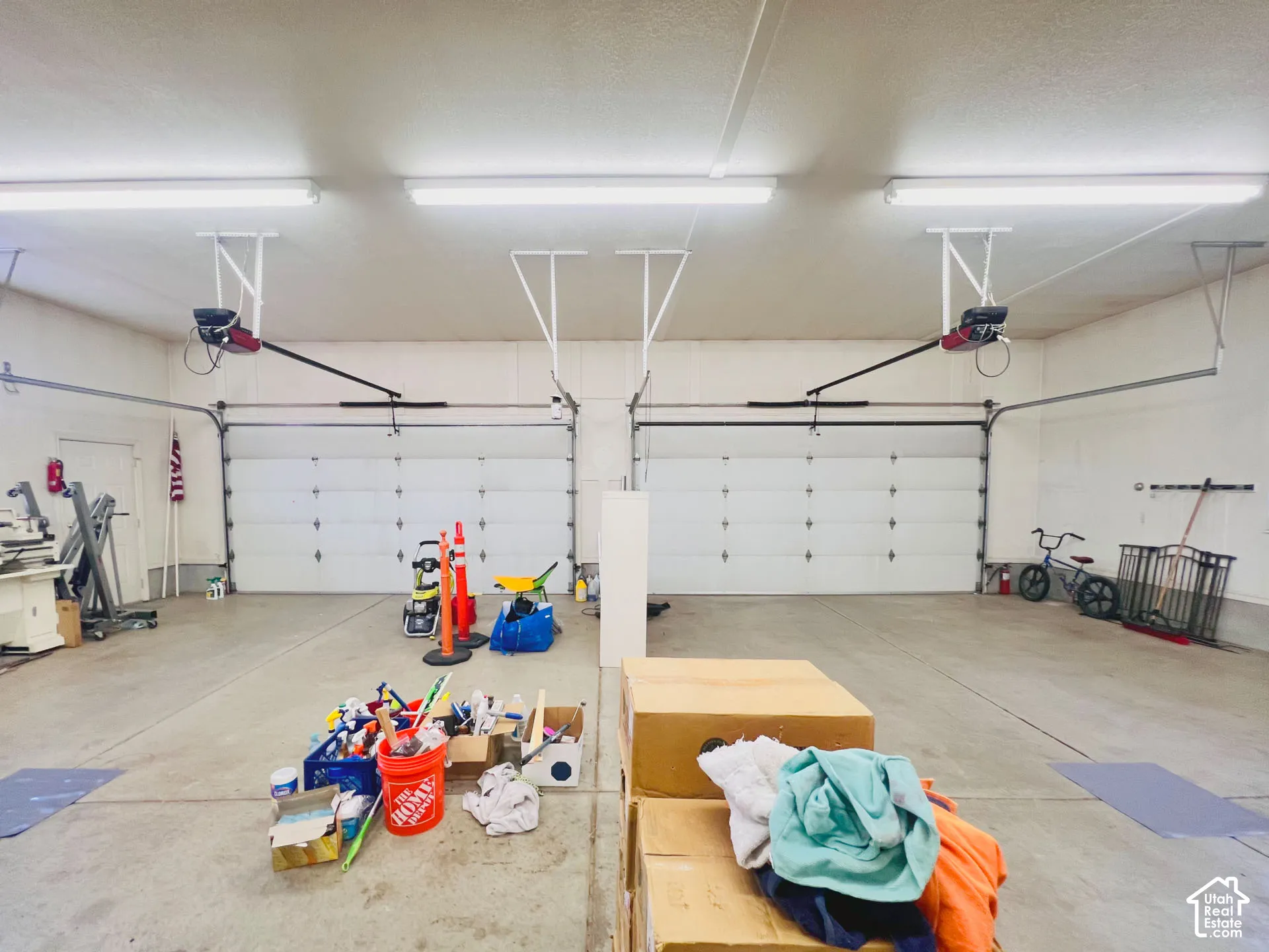 Two white panel garage doors, concrete flooring, overhead fluorescent lighting, and white painted walls