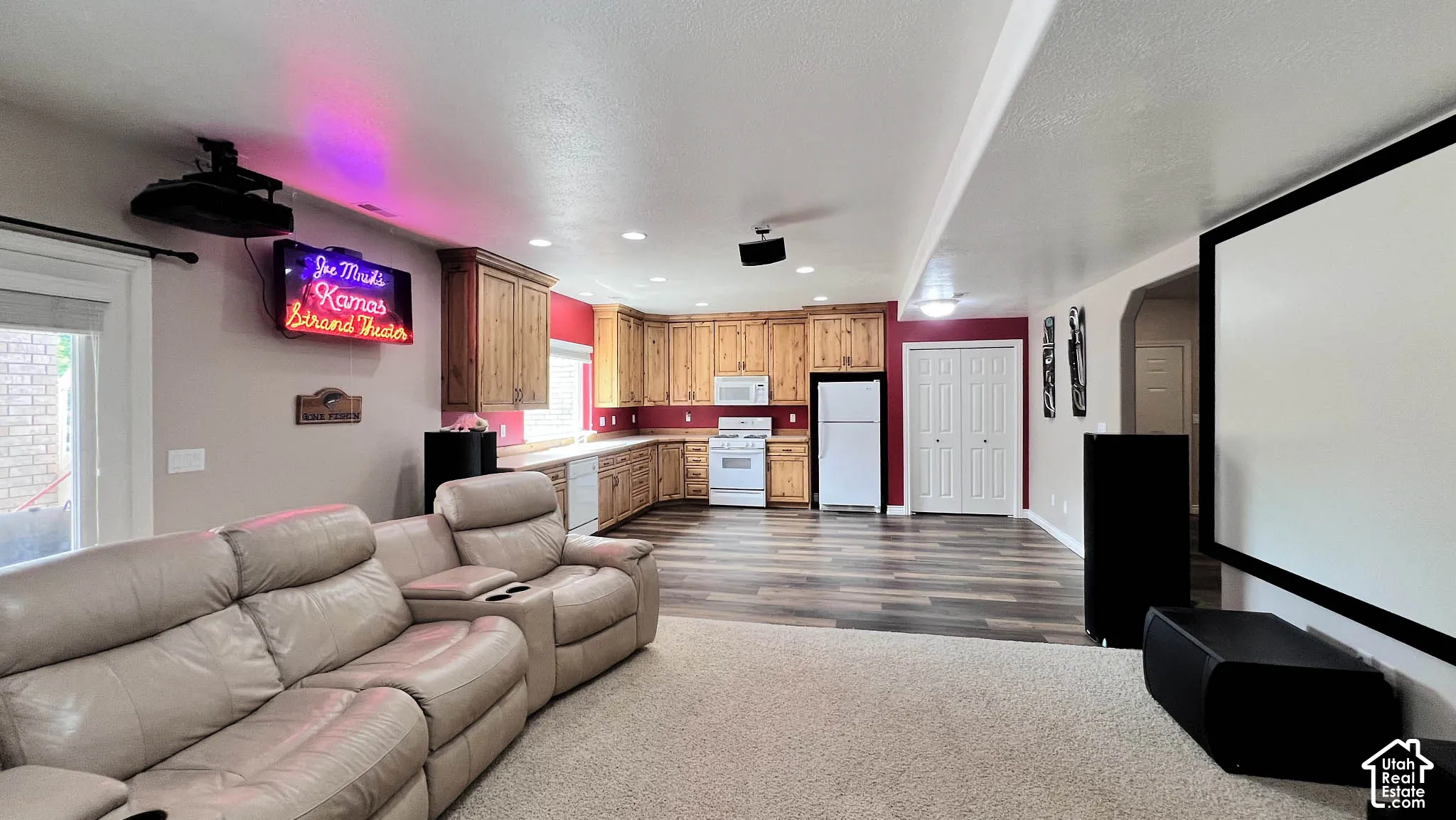 Projector with ceiling mount, large projection screen, wood-finish flooring, built-in kitchen cabinetry, and bifold closet doors