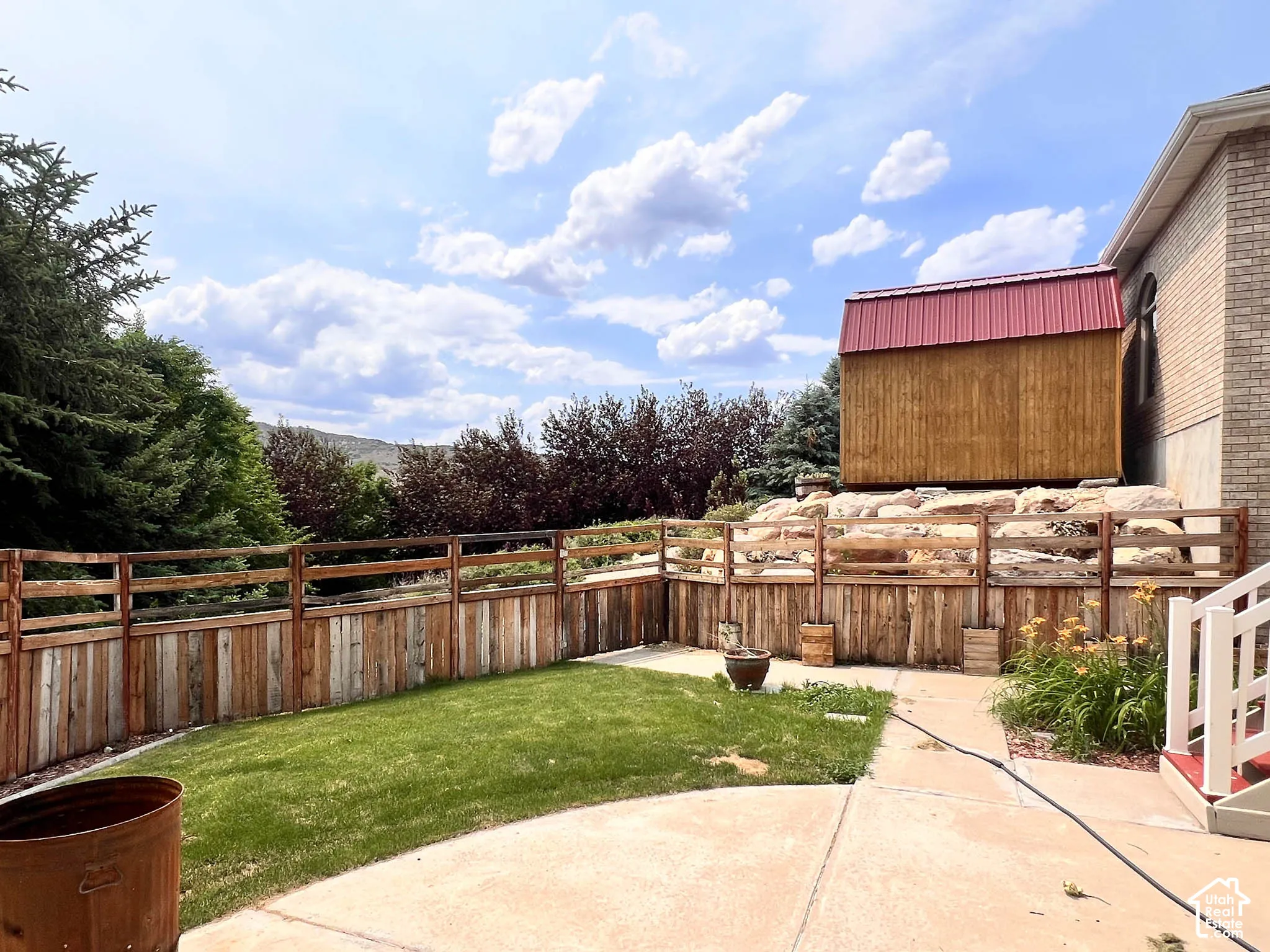 Expansive concrete patio with a tiered wooden fence and a separate wooden structure featuring a red metal roof