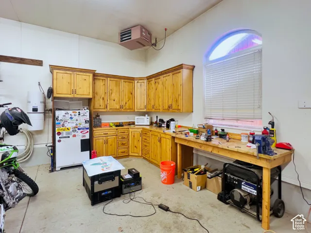Corner cabinetry with wood-finish doors, built-in workbench, arched window with horizontal blinds, and a wall-mounted heater