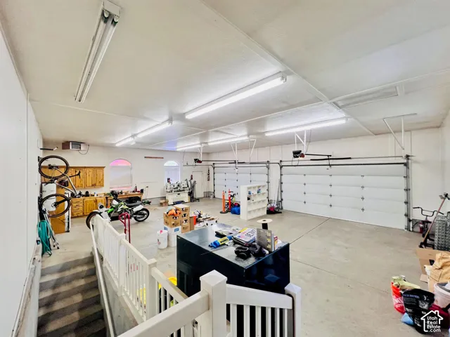 Concrete flooring, dual overhead garage doors, fluorescent lighting fixtures, built-in wooden cabinetry, and an arched window