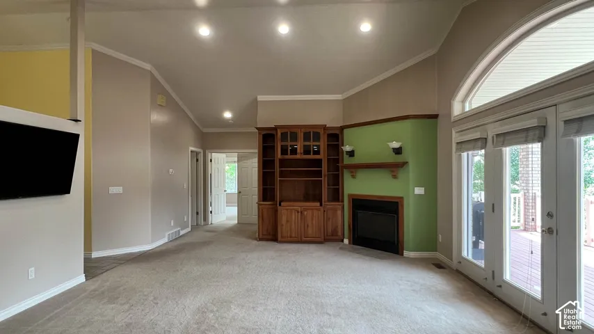 Spacious interior with vaulted ceilings, recessed lighting, built-in wooden cabinetry, a fireplace, and double glass panel doors with an arched transom window
