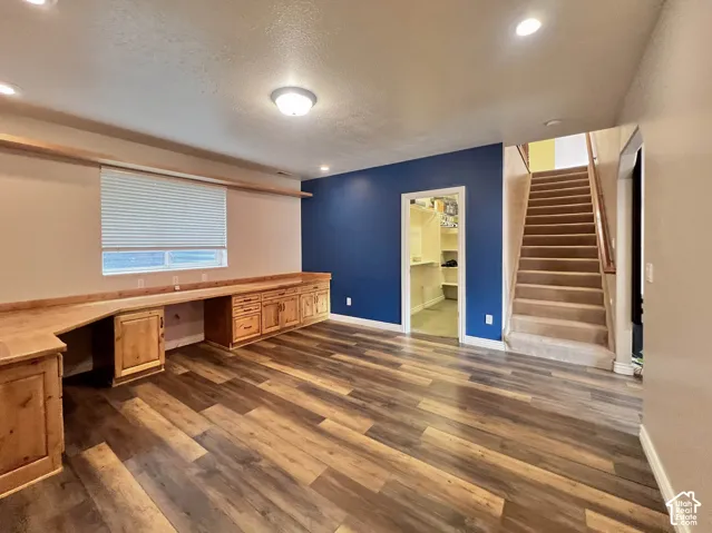 Wood-finish flooring, built-in wooden desk with integrated cabinetry, recessed lighting, and a carpeted staircase