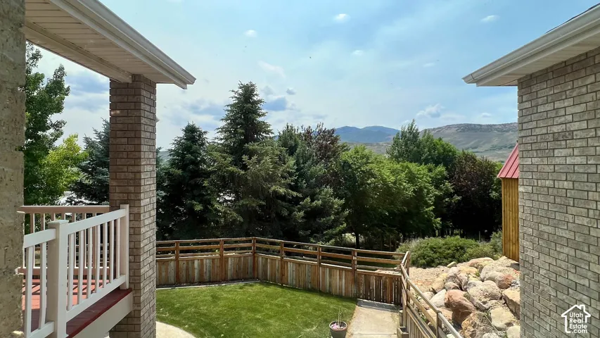 Brick exterior construction with white railing, wood fence, natural landscaping, and distant mountain scenery