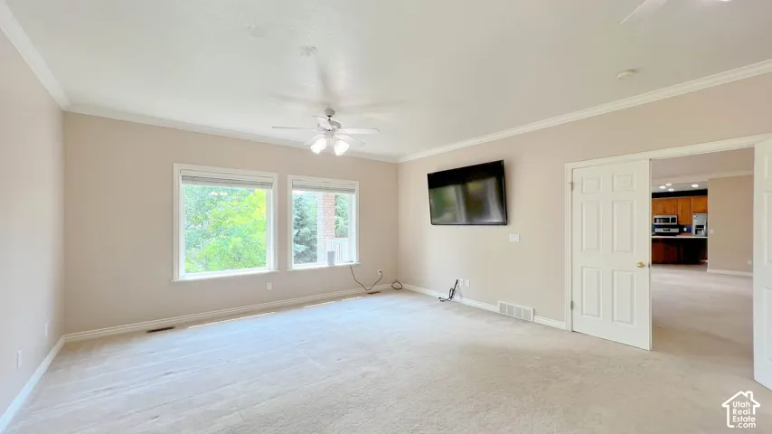 Spacious room with light-toned carpet flooring, two large windows, crown molding, and a ceiling fan