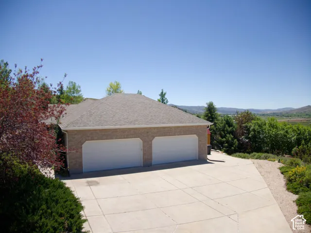 Brick exterior garage with two white garage doors, a concrete driveway, and surrounding greenery