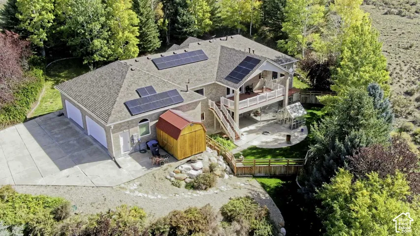 Pitched roof with solar panels, attached two-car garage, upper-level balcony, and a ground-level patio with a greenhouse
