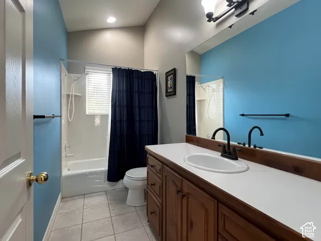 Integrated tub and shower combination, single vanity with wood-finish cabinetry, countertop with integrated sink, tile flooring, and overhead lighting