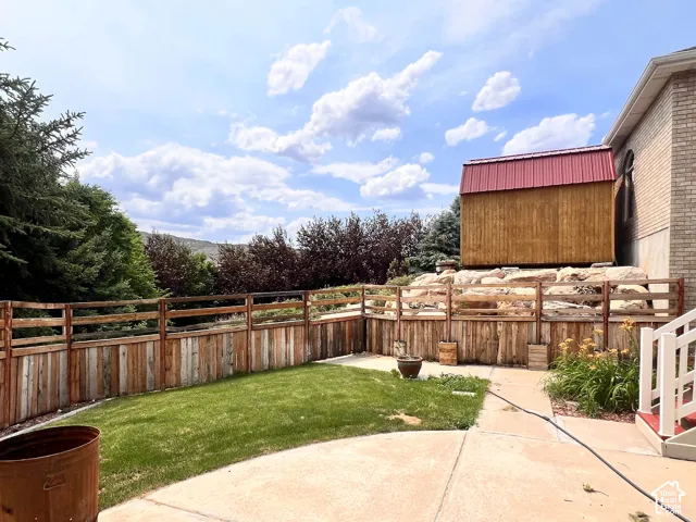 Expansive concrete patio with a tiered wooden fence and a separate wooden structure featuring a red metal roof