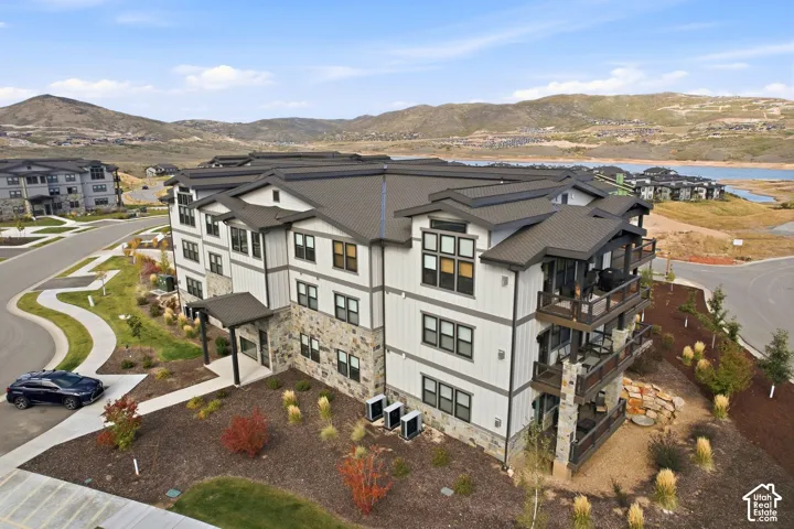 Multi-story building featuring a pitched roof, stone and siding exterior, multiple balconies, and integrated landscaping