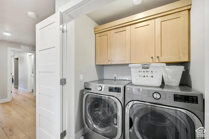 Laundry area featuring light wood-finish cabinetry, light gray walls, and light wood-finish flooring