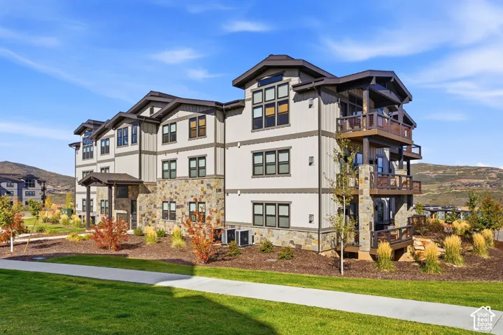 Multi-story exterior featuring a stone and siding facade, multiple balconies with railings, and a landscaped perimeter