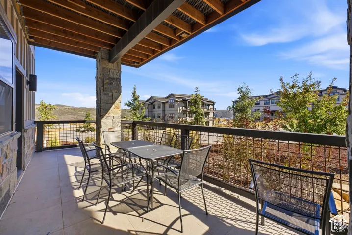 Covered patio with tile flooring, stone columns, wood-finish ceiling, and metal railings