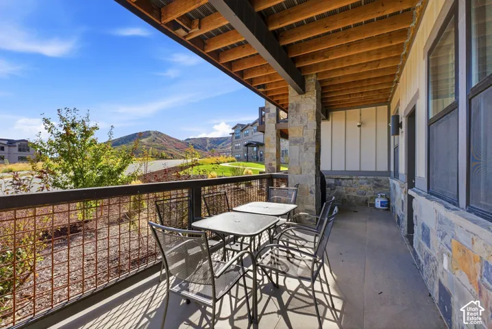 Covered patio with exposed wood ceiling beams, stone columns, and a metal railing