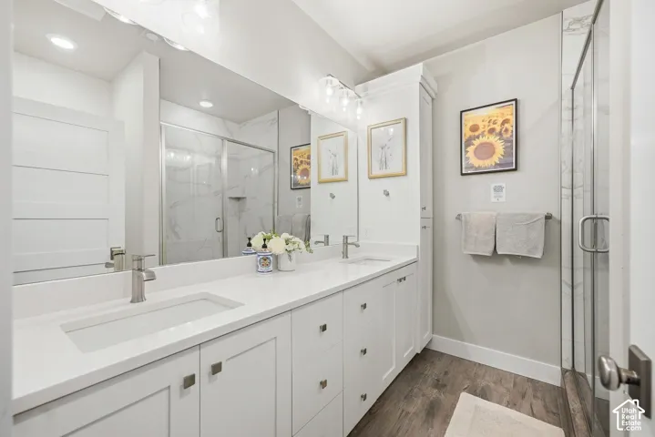 Double vanity with integrated sinks and brushed nickel faucets, white cabinetry, wood-finish flooring, and a glass-enclosed shower with a tiled surround