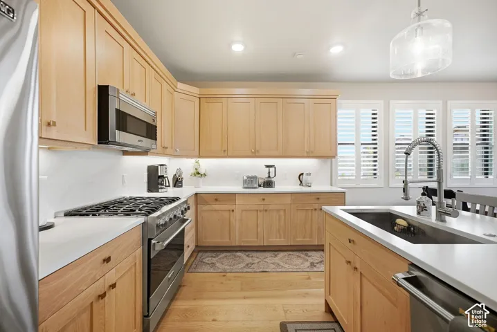 Kitchen featuring light wood cabinetry, stainless steel appliances, white countertops, and a kitchen island with an undermount sink