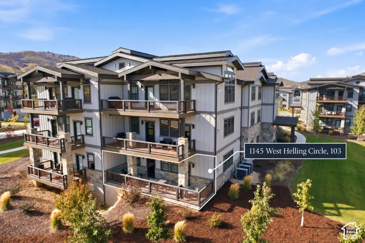 Multi-story building featuring stacked balconies with dark railings, stone accents, and light-colored siding