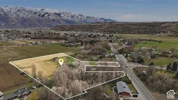 Expansive land parcel with surrounding agricultural fields, mature trees, and a distant mountain range backdrop